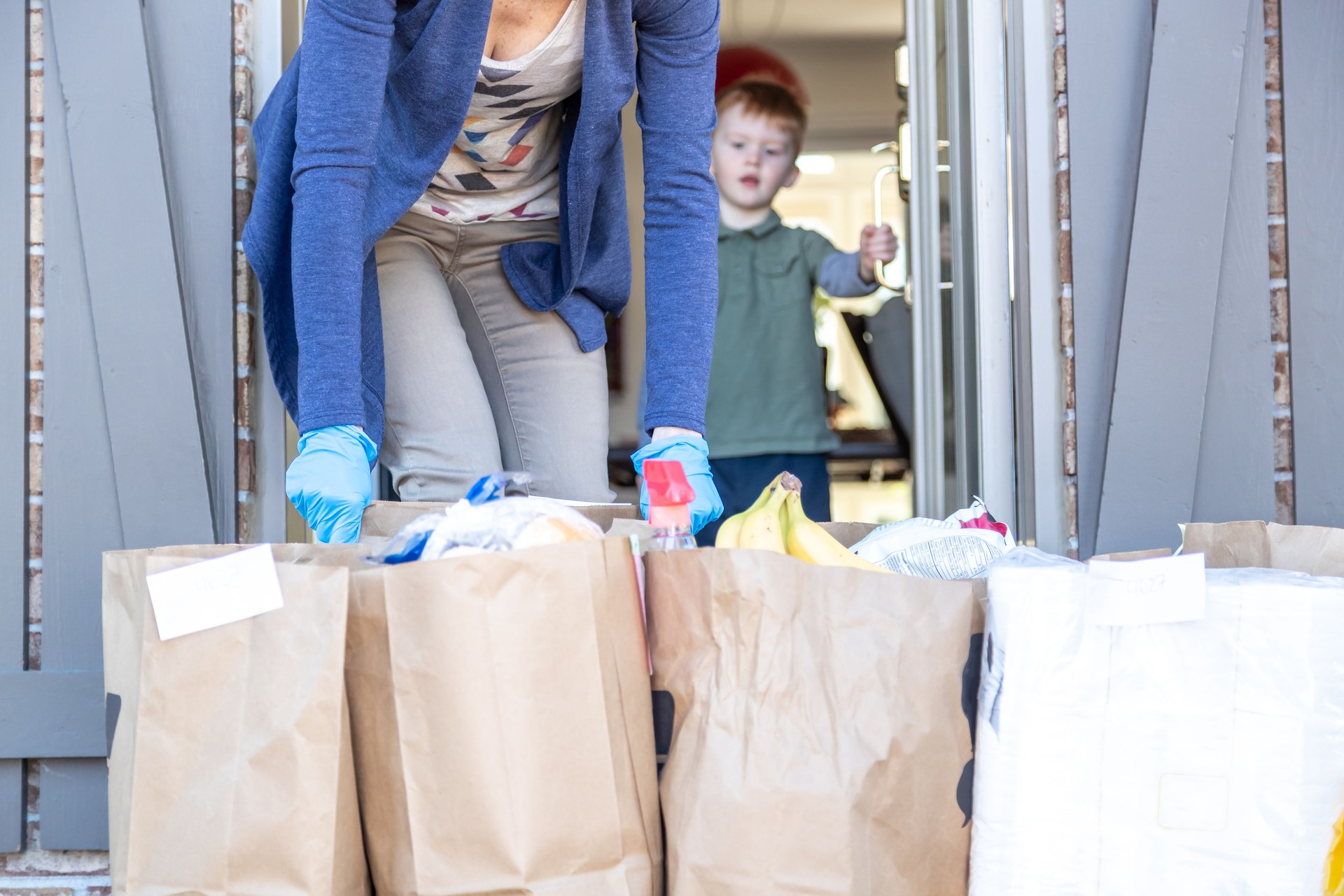 Woman taking in Grocery bags waiting outside at front door after delivery